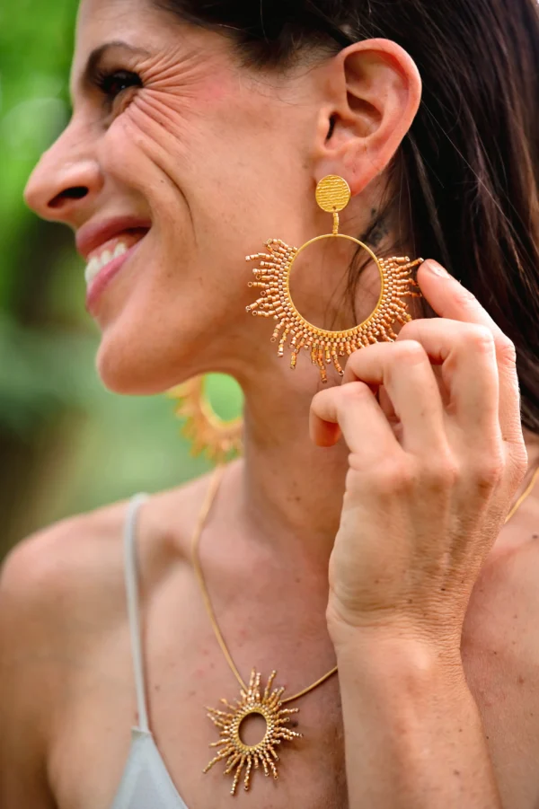 Femme souriante portant les boucles Apollisia Solaris Valdyria en perles Miyuki dorées plaqué or.