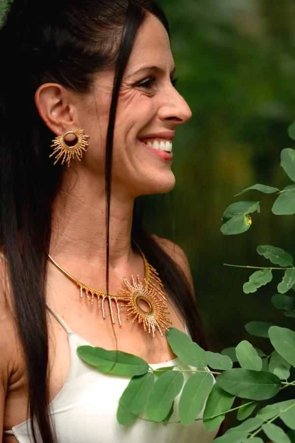 Femme souriante portant le collier Apollisia Solaris dans un décor verdoyant.