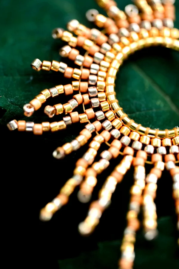 Gros plan sur les perles Miyuki dorées du collier sautoir Apollisia Solaris, en forme de soleil rayonnant.