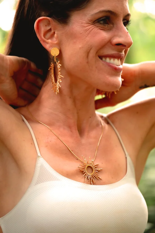 Le collier sautoir solaire est porté de profil, mettant en valeur son pendentif circulaire rayonnant.