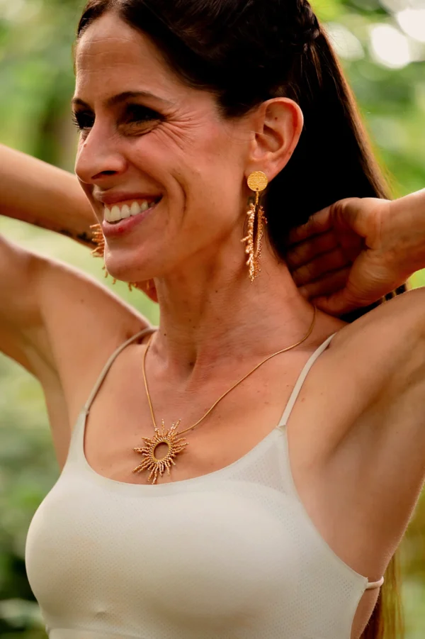 Le collier sautoir doré est porté à l’extérieur, capturant la lumière naturelle côté gauche.