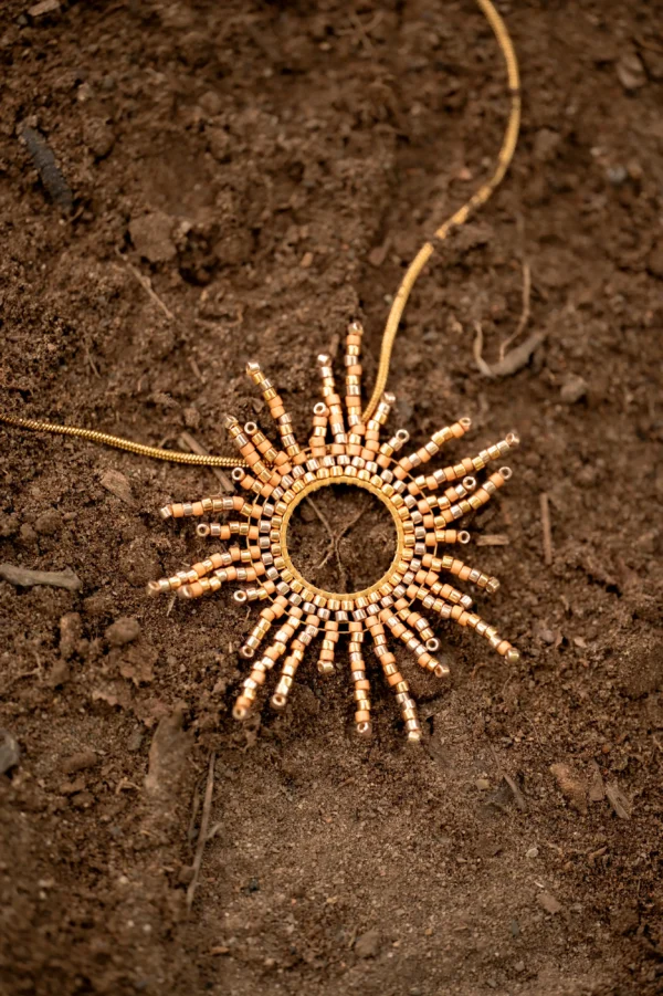 Photo du collier sautoir Apollisia Solaris posé à plat sur un sol brun, en vue produit.