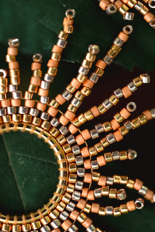 Petites boucles d’oreilles artisanales dorées avec perles Miyuki, posées sur une feuille.