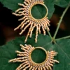 Paire de boucles d’oreilles dorées en perles Miyuki, en forme de soleil, présentées sur une feuille verte.