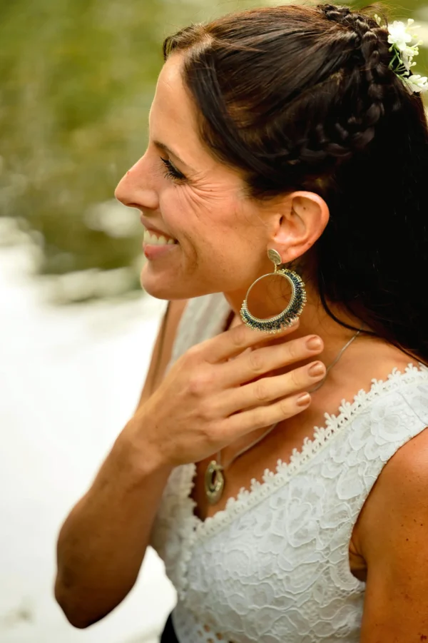 Femme assise au bord d’un lac portant les boucles Artemesia Lunaris Valdyria en perles Miyuki argent et bleu. Bijou artisanal fait main en Alsace, inspiré de la lune et de la nature.