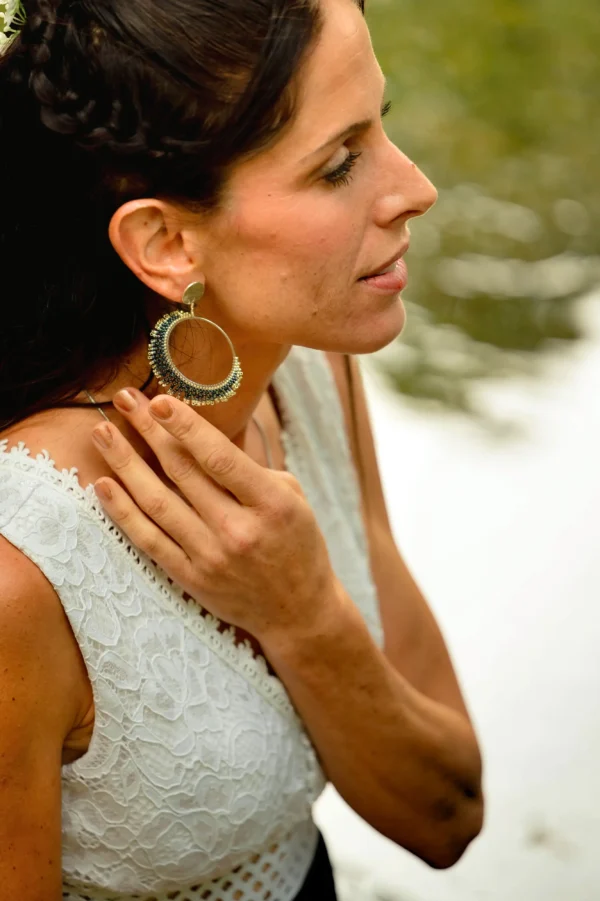 Boucles d’oreilles Artemesia Lunaris Valdyria portées par une femme posant la main sur son cou. Bijoux artisanaux en perles Miyuki argentées et bleues, inspirés par la lune.