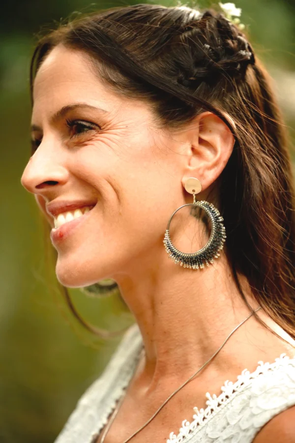 Femme souriante portant les boucles d’oreilles Artemesia Lunaris Valdyria, en perles Miyuki argent et bleu, bijou artisanal fait main inspiré de la lune.