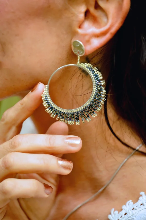 Boucle d’oreille pendante Artemesia Lunaris Valdyria portée à l’oreille d’une femme, main effleurant le bijou. Bijou artisanal en perles Miyuki argent et bleu, fait main en Alsace, inspiré par la lune.
