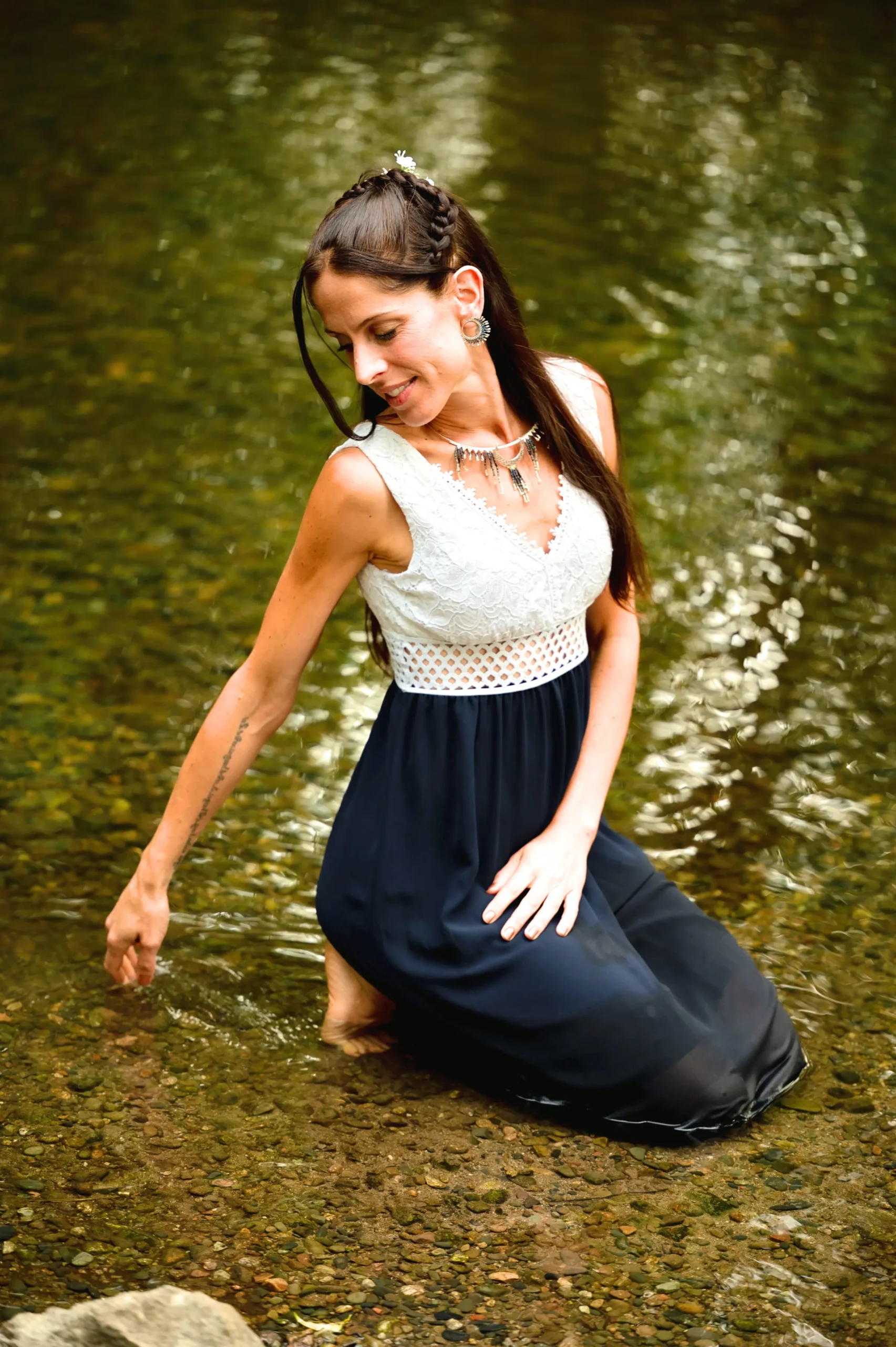Femme riant en jouant dans l’eau, portant le collier Majestueux Artemesia Lunaris Valdyria en perles Miyuki noir, or et argent. Bijou artisanal fait main.
