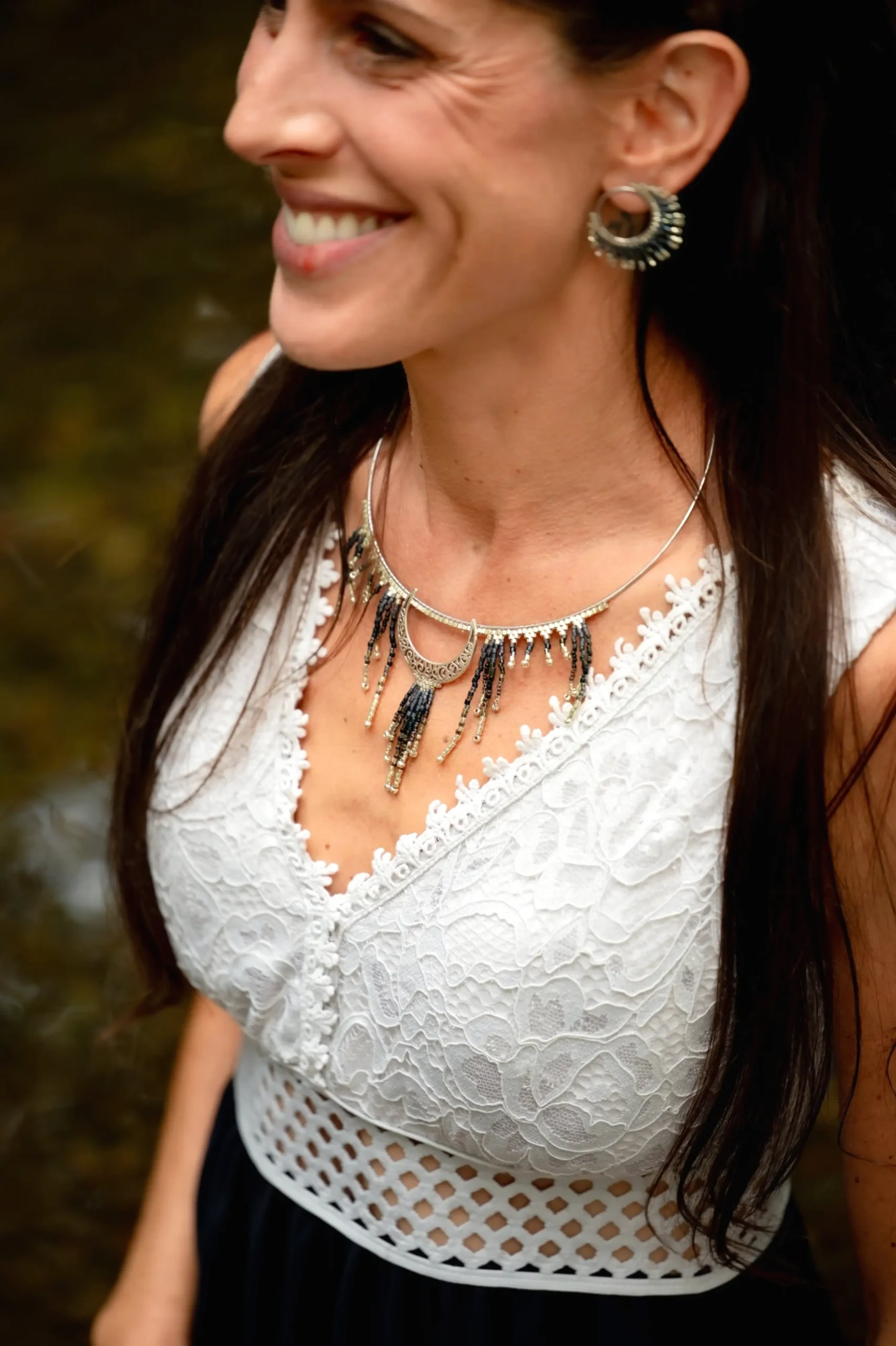 Femme assise en robe noire et blanche portant le collier Majestueux Artemesia Lunaris Valdyria. Bijou artisanal fait main en Alsace, en perles Miyuki noir, doré et argent.