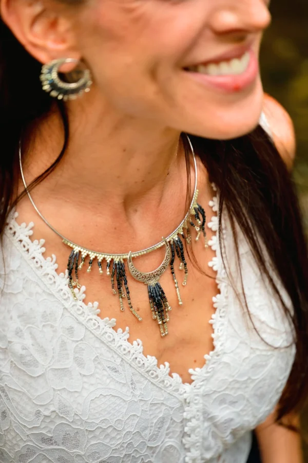 Femme souriante de profil portant le collier Majestueux Artemesia Lunaris Valdyria en perles Miyuki noir, doré et argent. Bijou artisanal fait main.