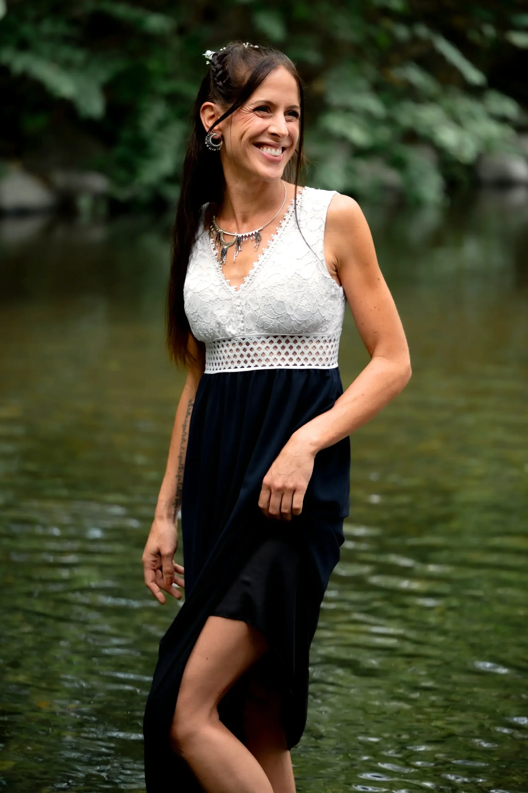 Femme debout au bord de l’eau portant les petites boucles Artemesia Lunaris Valdyria, en perles Miyuki bleu et argent. Bijou artisanal fait main en Alsace.