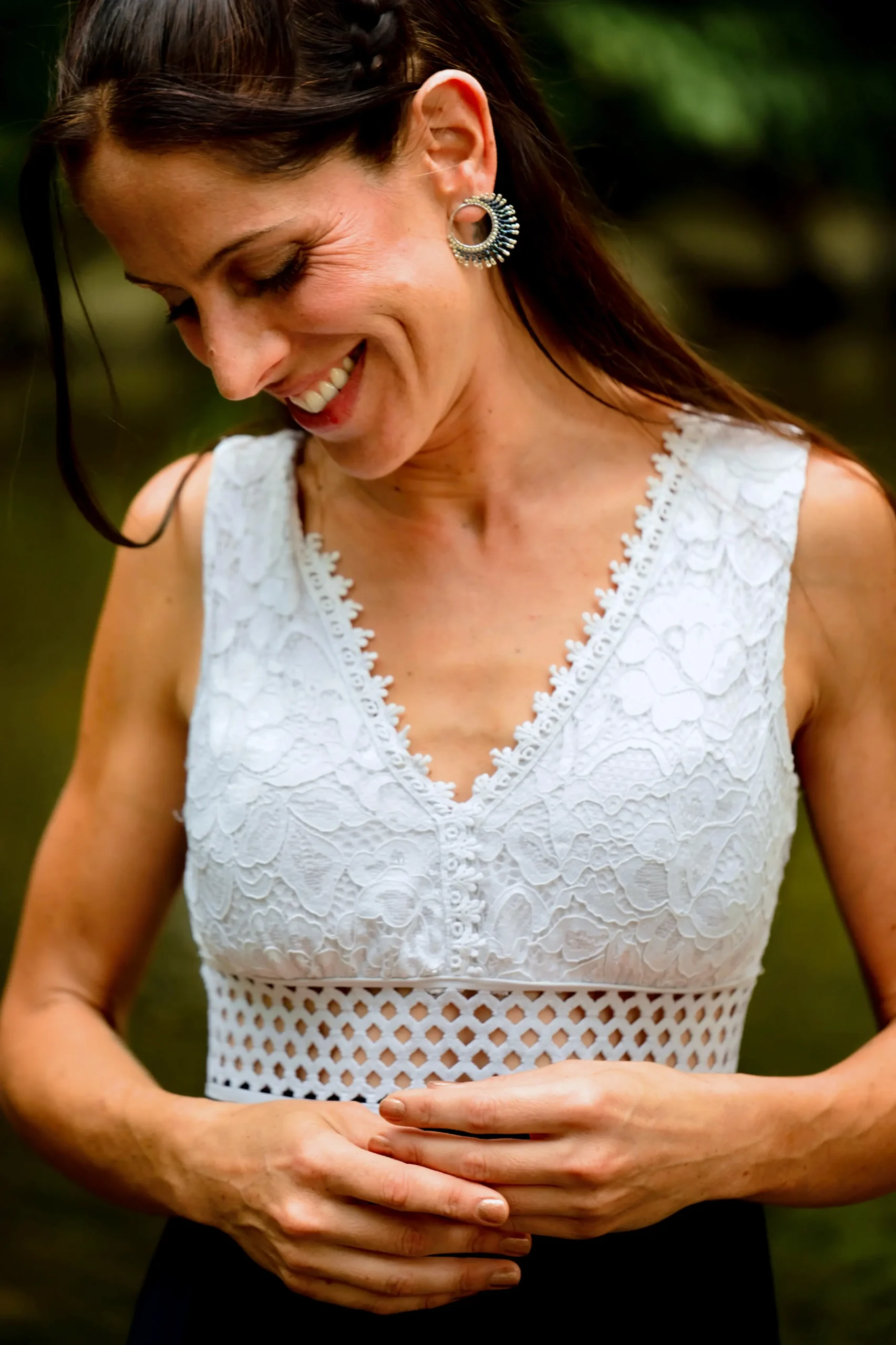 Femme souriante posant une main sur son cou, portant les petites boucles Artemesia Lunaris Valdyria. Bijou artisanal en perles Miyuki fait main en Alsace.