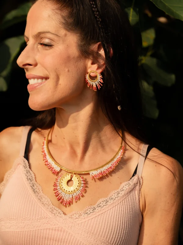 Femme souriante portant les petites boucles Mira Aurora Valdyria, perles Miyuki rose clair et foncé, cercle doré. Bijou artisanal made in France, parure lumineuse.