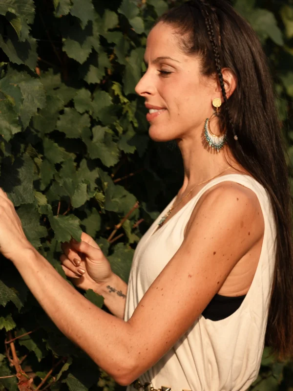Femme portant les boucles Mira Calypsa Valdyria, perles Miyuki turquoise et vert d’eau, monture dorée, dans la végétation. Bijoux artisanaux écoresponsables, inspirés par la mer et la nature.