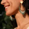 Femme souriante portant les boucles Mira Calypsa Valdyria, perles Miyuki turquoise et vert d’eau, monture dorée. Bijoux artisanaux made in France, talisman de joie.