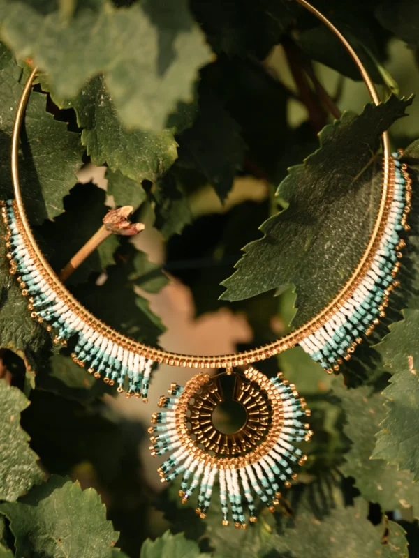 Collier Majestueux Mira Calypsa Valdyria, cercle doré orné de perles Miyuki turquoise et vert d’eau, posé près d’une feuille. Bijou artisanal alsacien, création consciente et symbolique.