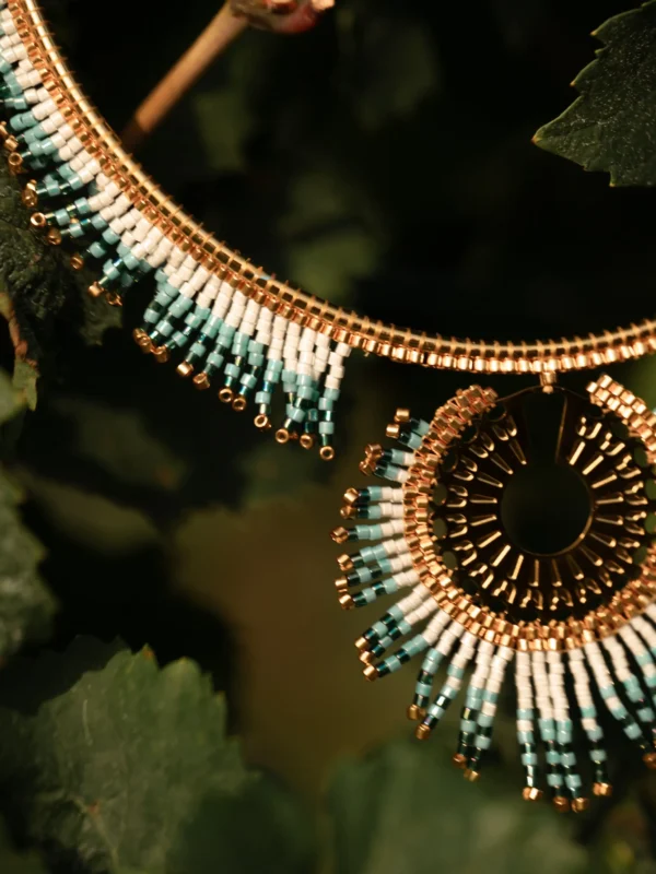 Collier Majestueux Mira Calypsa Valdyria, tissé de perles Miyuki turquoise et vert d’eau, monture dorée, suspendu dans les feuilles. Bijou artisanal français, durable et poétique.