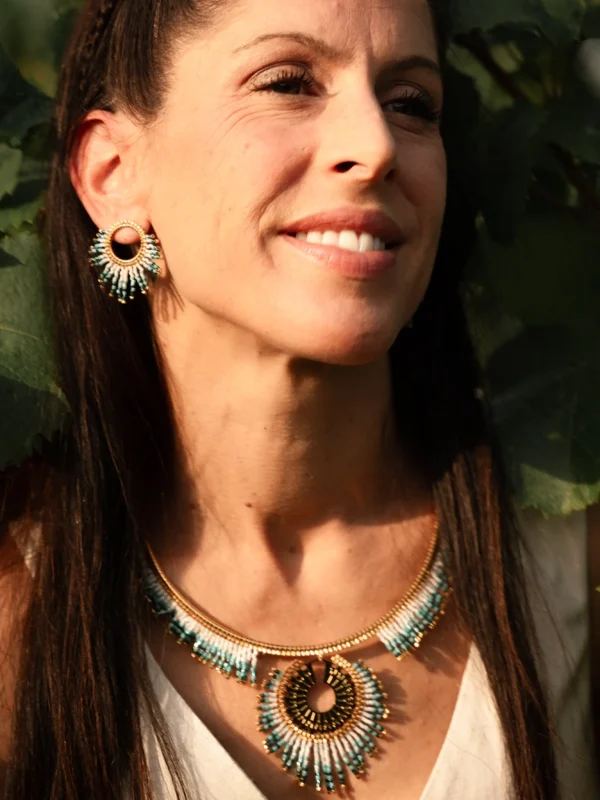 Femme souriante portant le Collier Majestueux Mira Calypsa Valdyria, perles Miyuki turquoise et vert d’eau, monture dorée. Bijou artisanal fait main, durable et lumineux.