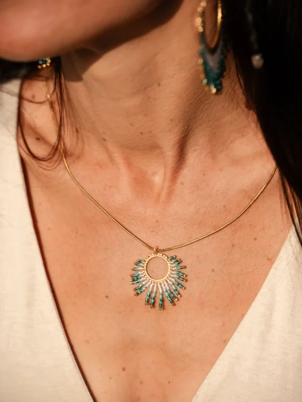 boutique-valdyria-mira-calypsa-collier-sautoir-porté-profil Collier Sautoir Mira Calypsa Valdyria, pendentif circulaire doré orné de perles Miyuki turquoise et blanches, porté au cou, gros plan de profil. Bijou artisanal français, durable et raffiné.