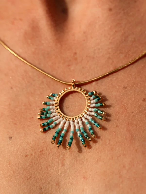 boutique-valdyria-mira-calypsa-collier-sautoir-porté-gros-plan Collier Sautoir Mira Calypsa Valdyria, pendentif doré orné de perles Miyuki turquoise et blanches, porté autour du cou. Bijou artisanal made in France, mystique et raffiné.