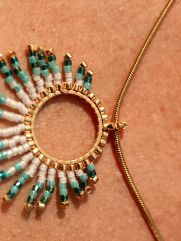 boutique-valdyria-mira-calypsa-collier-sautoir-pendentif-gros-plan Collier Sautoir Mira Calypsa Valdyria, pendentif circulaire doré tissé de perles Miyuki turquoise et blanches, gros plan sur cordon doré. Bijou artisanal écoresponsable, fait main en Alsace.