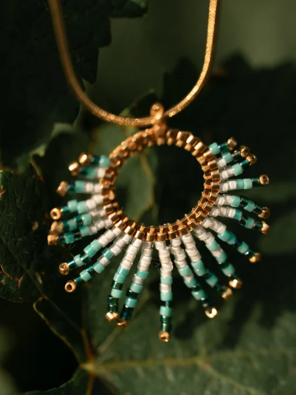 boutique-valdyria-mira-calypsa-collier-sautoir-feuillage Collier Sautoir Mira Calypsa Valdyria, pendentif doré orné de perles Miyuki turquoise et blanches, suspendu dans les feuilles. Bijou artisanal fait main en Alsace, inspiré par la nature.