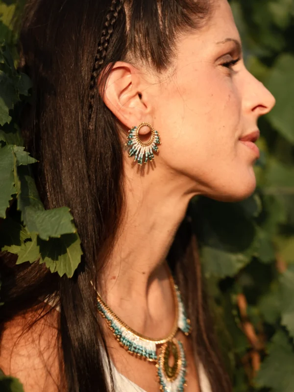 Petites boucles Mira Calypsa Valdyria, portées à l’oreille, perles Miyuki turquoise et blanches, monture dorée, lumière douce dans les vignes. Bijou artisanal français, durable et poétique.