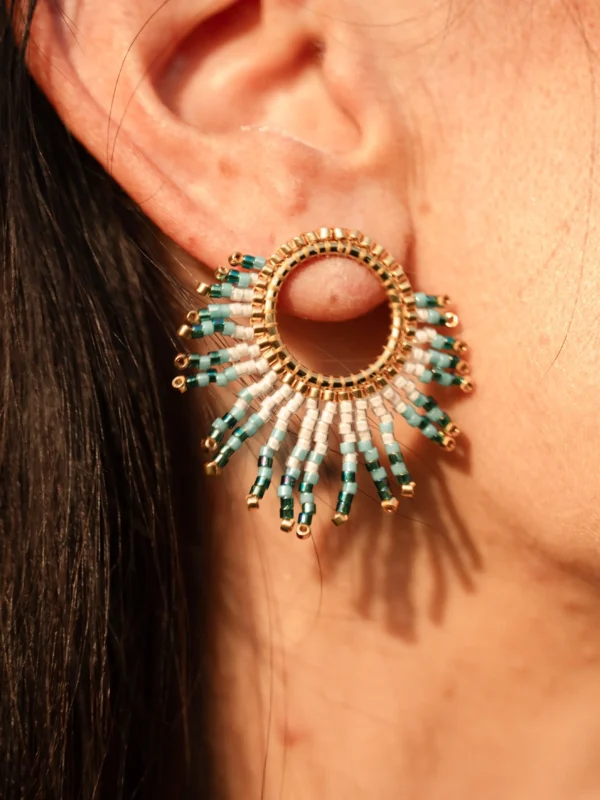 Portrait de femme portant la petite boucle Mira Calypsa Valdyria, perles Miyuki turquoise et blanches, monture dorée. Bijou artisanal fait main en Alsace, élégant et intemporel.