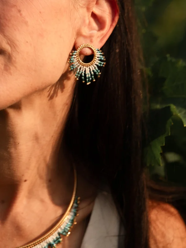 Petite boucle Mira Calypsa Valdyria, perles Miyuki turquoise et blanches, monture dorée, portée à l’oreille en profil droit. Bijou artisanal fait main, durable et élégant.