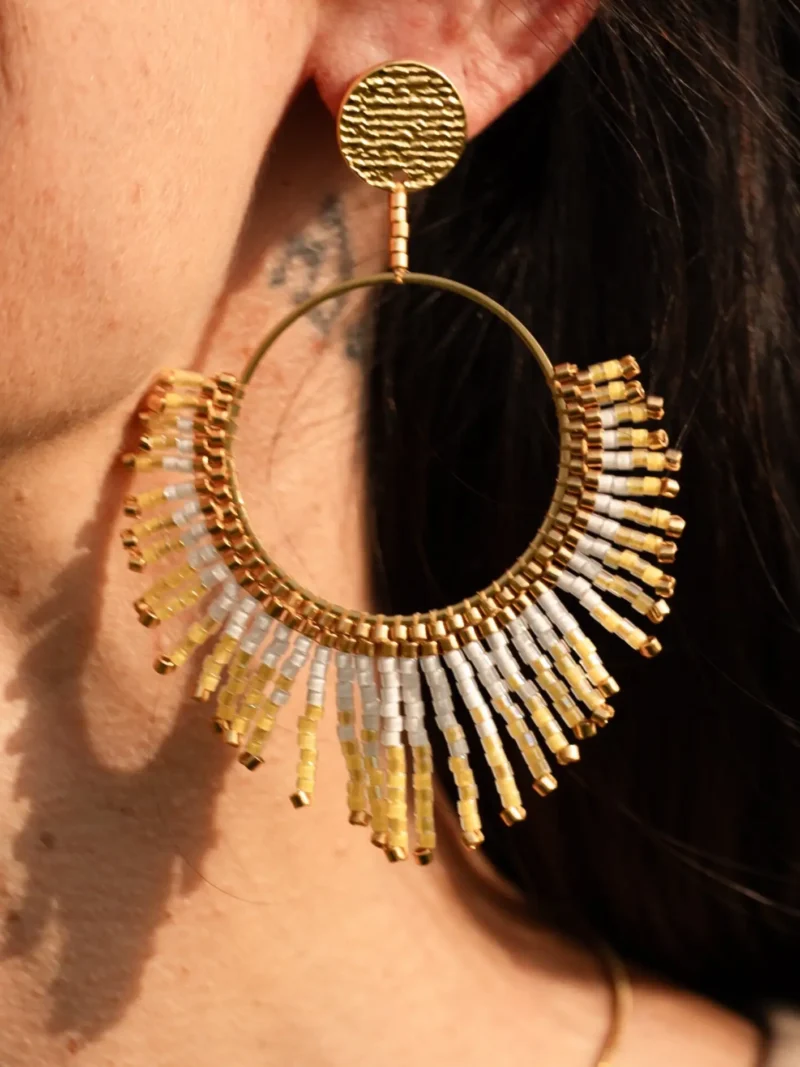 boutique-valdyria-mira-helia-boucle-oreille-pendante-gros-plan Boucle d’oreille pendante Mira Helia en perles Miyuki dorées et blanches, présentée en gros plan. Bijou artisanal français, fait main en Alsace, création durable et poétique inspirée du soleil.