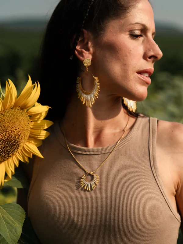 boutique-valdyria-mira-helia-boucles-oreilles-pendantes-portrait-tournesol Boucles d’oreilles pendantes Mira Helia en perles Miyuki dorées et blanches, portées avec le collier sautoir assorti, portrait avec tournesol. Bijoux artisanaux français, faits main en Alsace, créations éthiques et solaires.