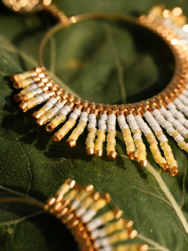 boutique-valdyria-mira-helia-boucles-oreilles-pendantes-feuille-verte Boucles d’oreilles pendantes Mira Helia en perles Miyuki dorées et blanches, posées sur une feuille verte. Bijoux artisanaux français, faits main en Alsace, créations durables inspirées du soleil.