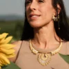 Portrait féminin avec collier majestueux Mira Helia en perles Miyuki dorées et blanches, porté dans un champ de tournesols. Bijou artisanal fait main en Alsace, création écoresponsable inspirée du soleil.