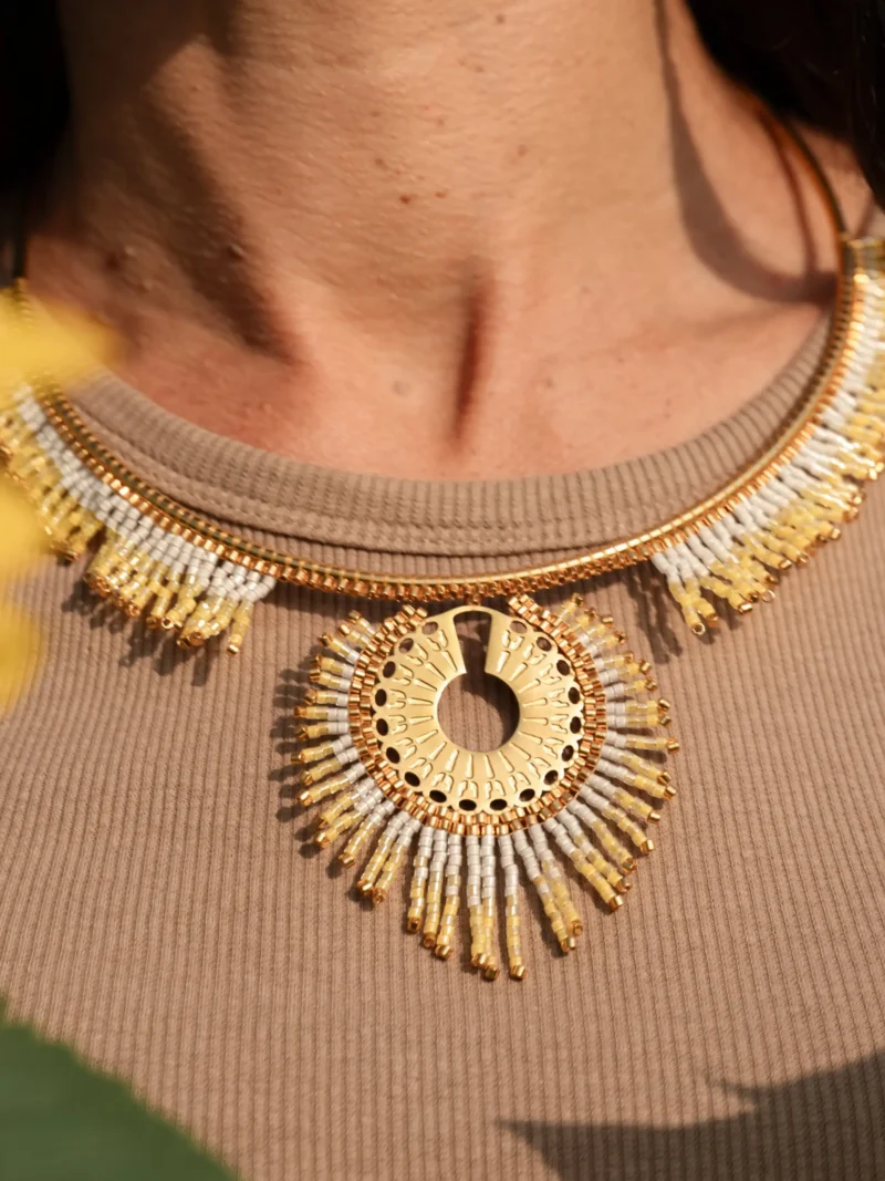 boutique-valdyria-mira-helia-collier-majestueux-gros-plan-soleil Gros plan sur le collier majestueux Mira Helia en perles Miyuki dorées et blanches, tissé à la main dans l’atelier Valdyria en Alsace. Bijou artisanal français, création écoresponsable et inspirée du soleil.