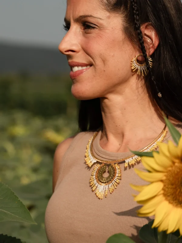 Portrait latéral d’une femme portant le collier Mira Helia et ses boucles d’oreilles dorées, réalisés en perles Miyuki japonaises. Bijou artisanal français, fait main en Alsace, création durable inspirée du soleil.