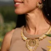 Portrait de profil d’une femme portant le collier majestueux Mira Helia et ses boucles assorties en perles Miyuki dorées et blanches. Bijou artisanal français, confectionné à la main en Alsace, création écoresponsable inspirée du soleil.