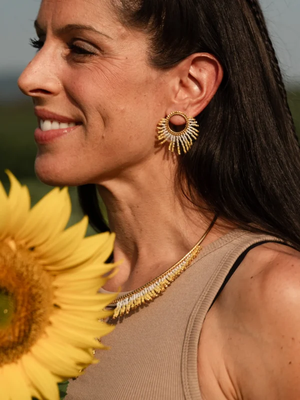 boutique-valdyria-mira-helia-petite-boucle-oreille-parure-majestueuse Petite boucle d’oreille Mira Helia en perles Miyuki dorées et blanches, portée avec le collier majestueux Mira Helia. Bijoux artisanaux français, faits main en Alsace, créations écoresponsables et solaires.