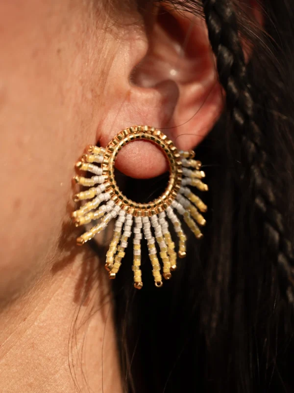 boutique-valdyria-mira-helia-petite-boucle-oreille-portee-gros-plan Petite boucle d’oreille Mira Helia en perles Miyuki dorées et blanches, portée à l’oreille en gros plan. Bijou artisanal français, fait main en Alsace, création durable et poétique.