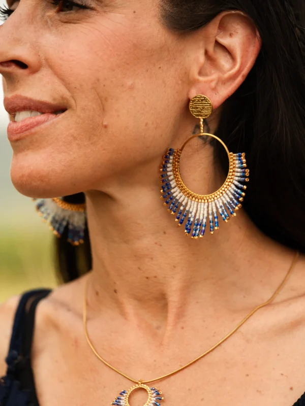 Boucles d’oreilles pendantes Mira Obscura en perles Miyuki bleu nuit, blanches et dorées, portées avec collier assorti. Bijoux artisanaux français, faits main en Alsace, créations éthiques et durables.