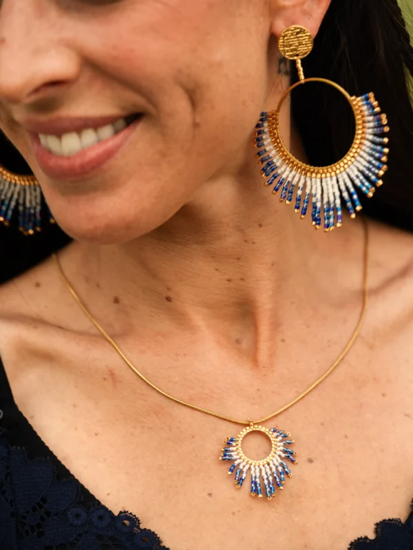 Boucle d’oreille pendante Mira Obscura en perles Miyuki bleues, blanches et dorées, portée en portrait rapproché avec sourire doux. Bijou artisanal français, fait main en Alsace, création durable et poétique.