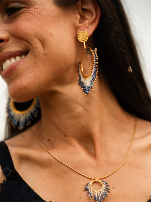 Boucles d’oreilles pendantes Mira Obscura en perles Miyuki bleu nuit et dorées, portées en portrait souriant. Bijoux artisanaux français, faits main en Alsace, créations durables et poétiques.