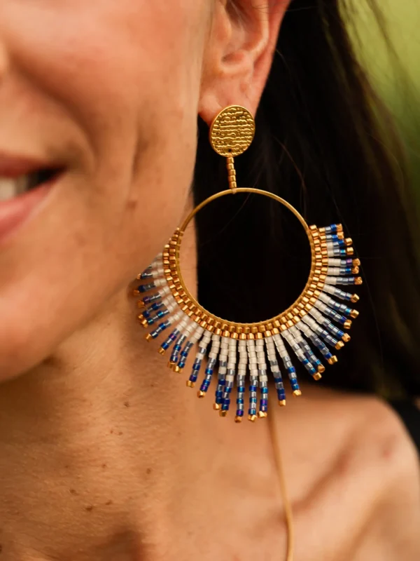 Boucle d’oreille pendante Mira Obscura en perles Miyuki bleues, blanches et dorées, portée en gros plan. Bijou artisanal français, fait main en Alsace, création durable et inspirée des astres.