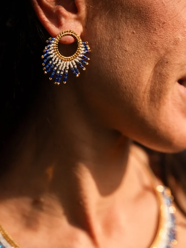 boutique-valdyria-mira-obscura-petite-boucle-oreille-portrait-joyeux Petite boucle d’oreille Mira Obscura en perles Miyuki bleues et dorées, portée en portrait souriant. Bijou artisanal français, fait main en Alsace, création durable et poétique.