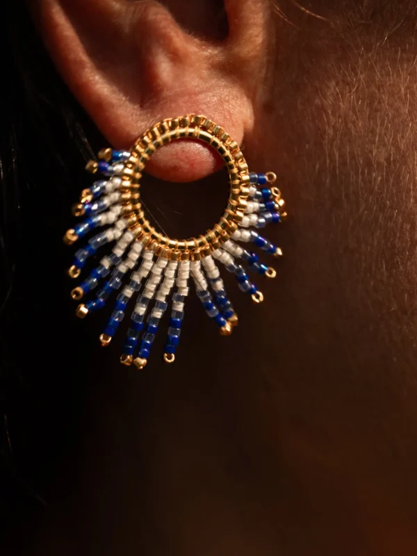 boutique-valdyria-mira-obscura-petite-boucle-oreille-gros-plan Petite boucle d’oreille Mira Obscura en perles Miyuki bleues, blanches et dorées, portée en gros plan. Bijou artisanal français, fait main en Alsace, création durable et poétique.
