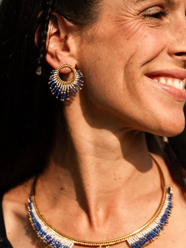 boutique-valdyria-mira-obscura-petites-boucles-oreilles-portrait-souriant Petite boucle d’oreille Mira Obscura en perles Miyuki bleu nuit, blanches et dorées, portée en portrait rapproché. Bijou artisanal français, fait main en Alsace, création durable et cosmique.