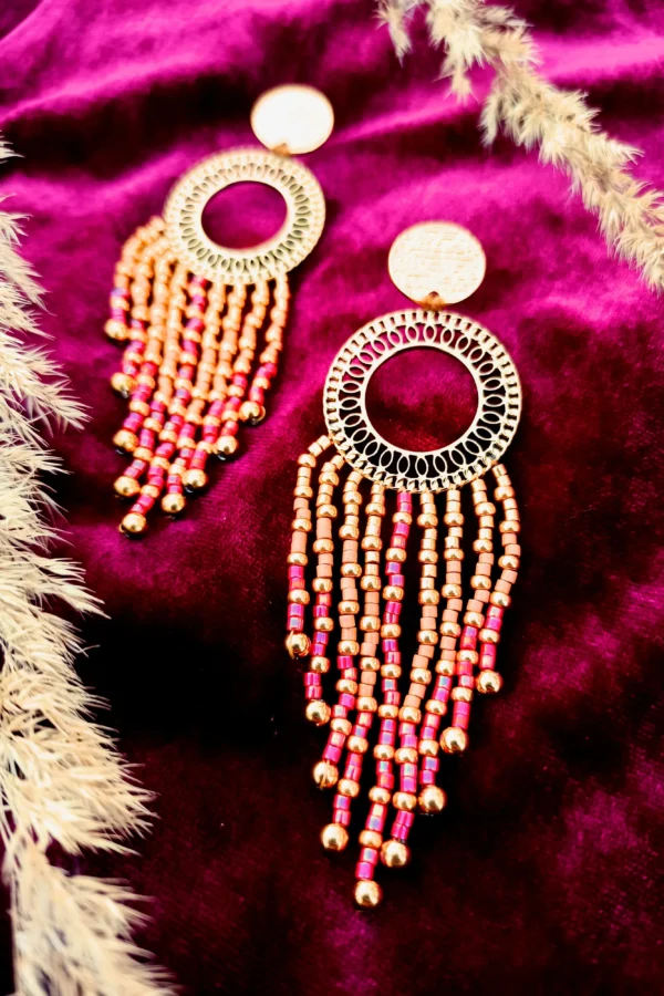 Grandes boucles d’oreilles Amaziga Rubra et talisman de vie Grandes boucles d’oreilles Amaziga Rubra posées avec perles roses et détails dorés artisanaux