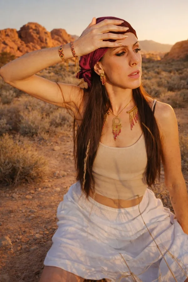 Collier majestueux Amaziga Rubra et ancrage féminin Collier majestueux Amaziga Rubra porté dans un paysage naturel aride avec perles roses et détails dorés