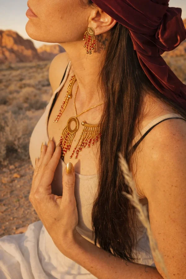 Collier majestueux Amaziga Rubra et geste du corps Femme touchant un collier majestueux Amaziga Rubra avec perles roses et détails artisanaux