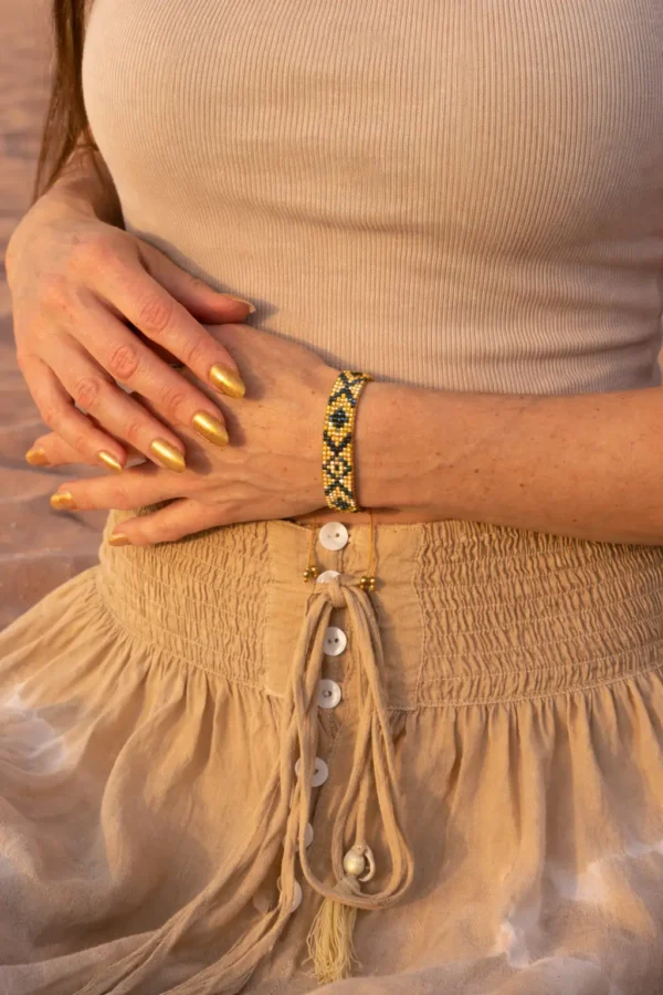 Bracelet bronze Amaziga Sacra porté au poignet dans un désert sous ciel bleu inspiré du Sahara